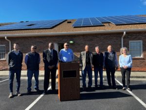 Eight clean energy leaders stand in front of a rooftop with solar panels to celebrate the solar installation.